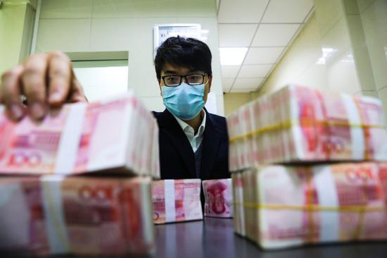 An employee of Lin'an Rural Commercial Bank counts banknotes at the bank's branch in Hangzhou, capital of Zhejiang province, on Feb 25. [Photo by Hu Jianhuan For China Daily]